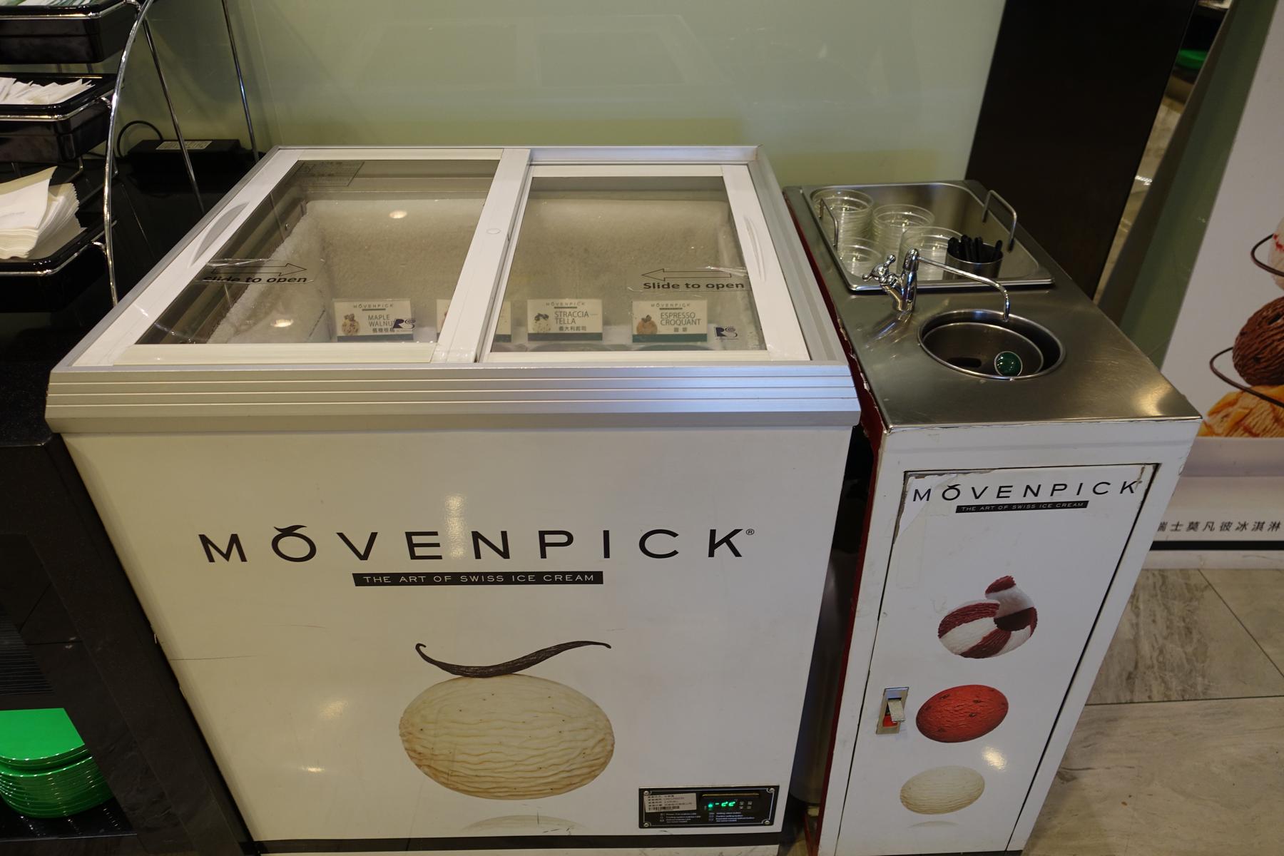 Movenpick ice cream freezer with visible flavors like Maple Walnut, Stracciatella, and Espresso Croquant, next to a scoop-washing station.