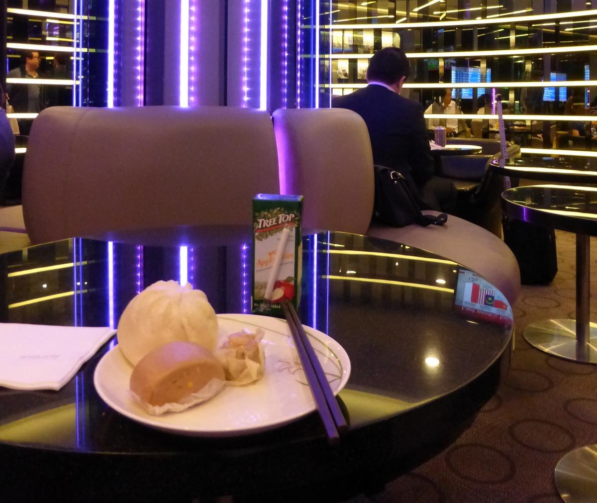 A plate of dim sum and an apple juice box sit on a glossy table in a modern lounge with purple accent lighting.