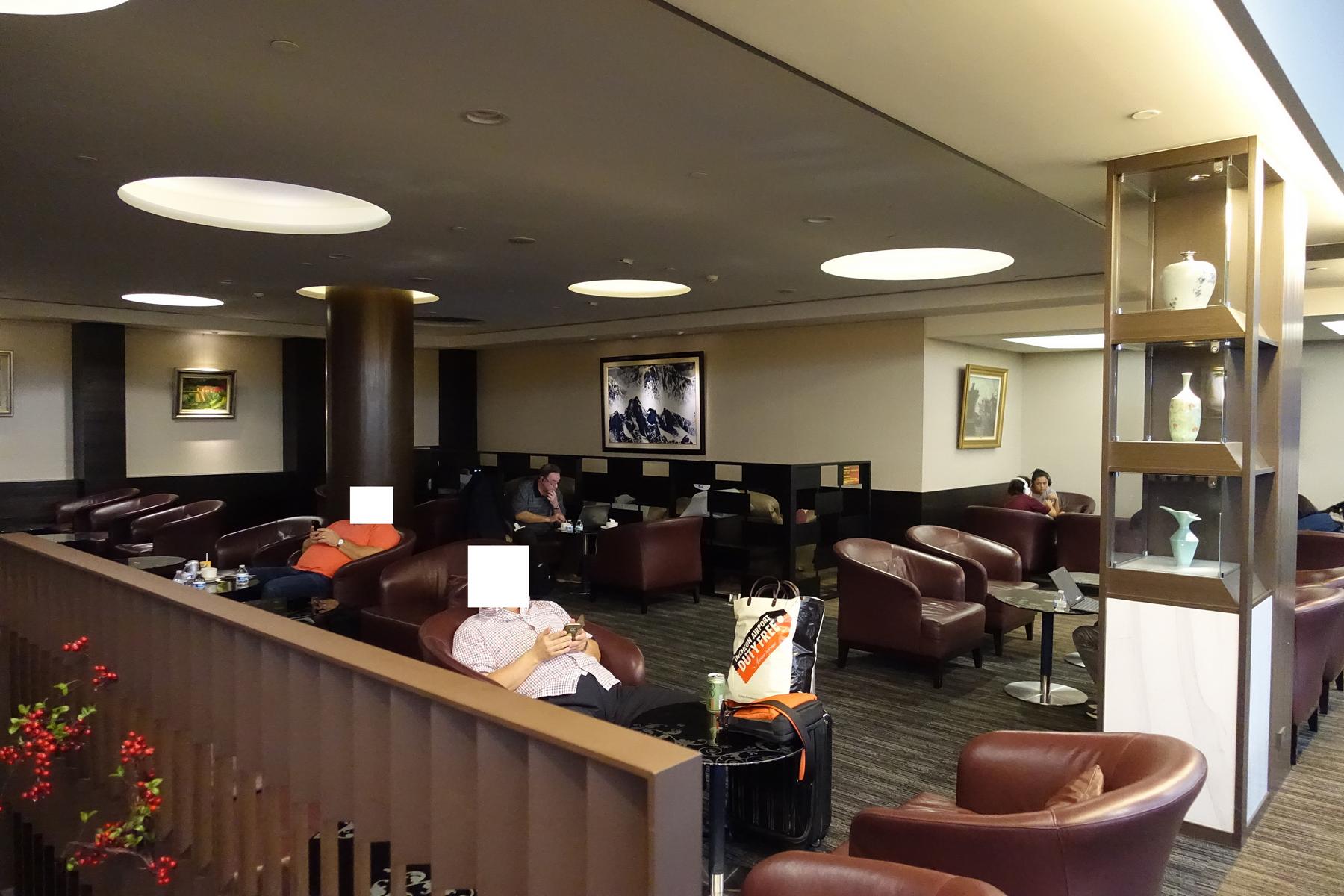 People relax in a spacious airport lounge with brown leather armchairs, paintings, and decorative vases.
