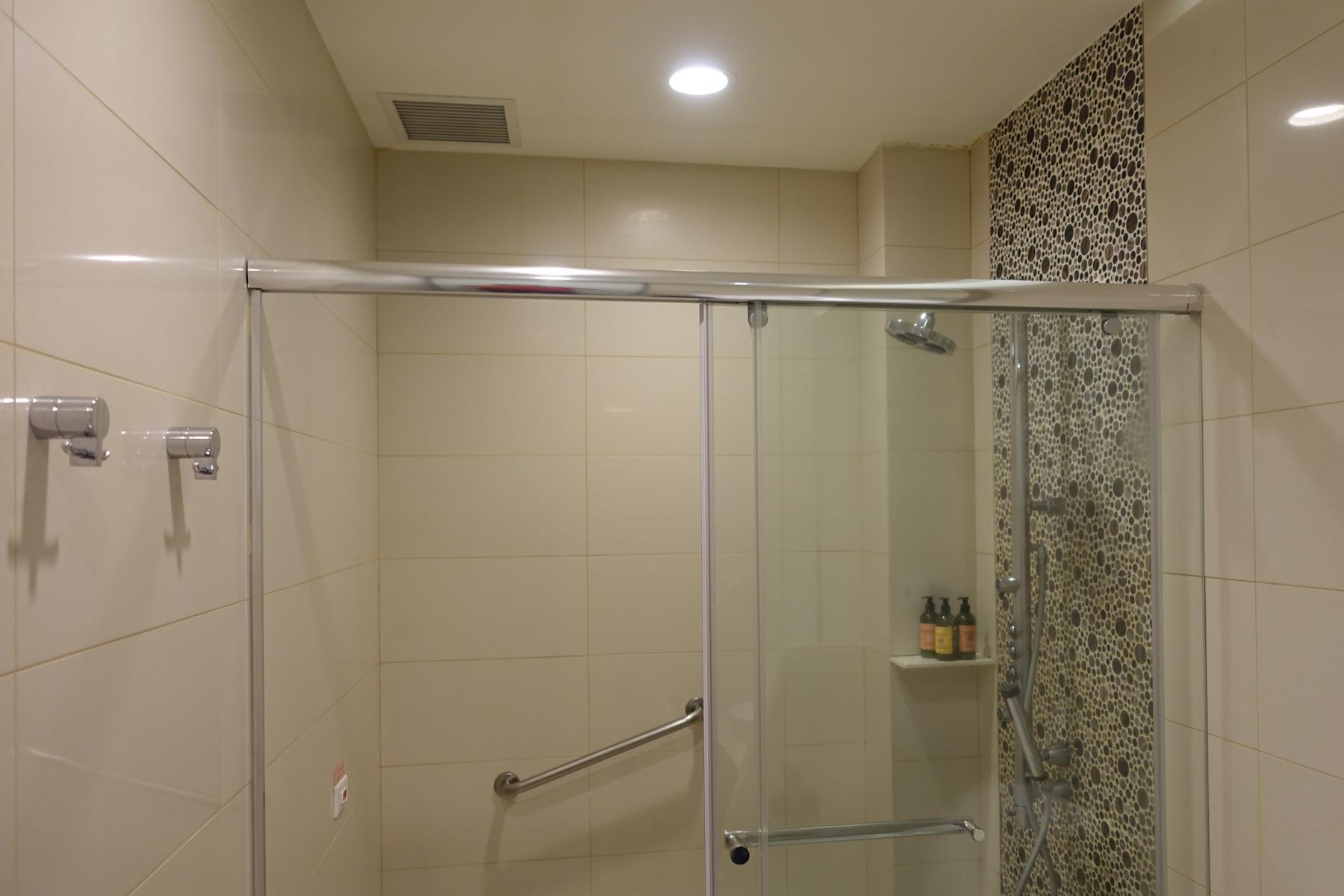 An empty modern shower stall with beige tiles, a glass sliding door, and a mosaic accent wall.