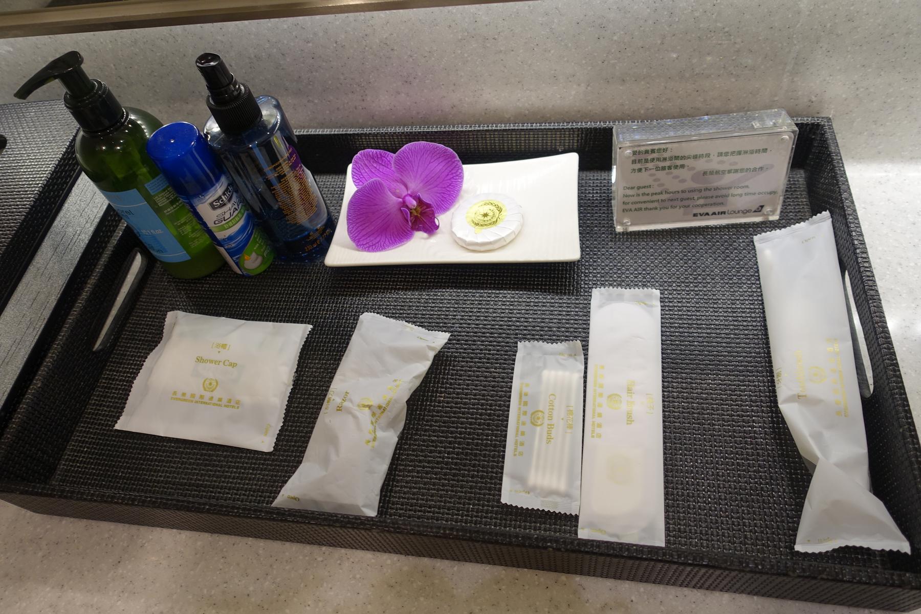 A black tray filled with shower amenities, toiletries, and a decorative purple orchid.