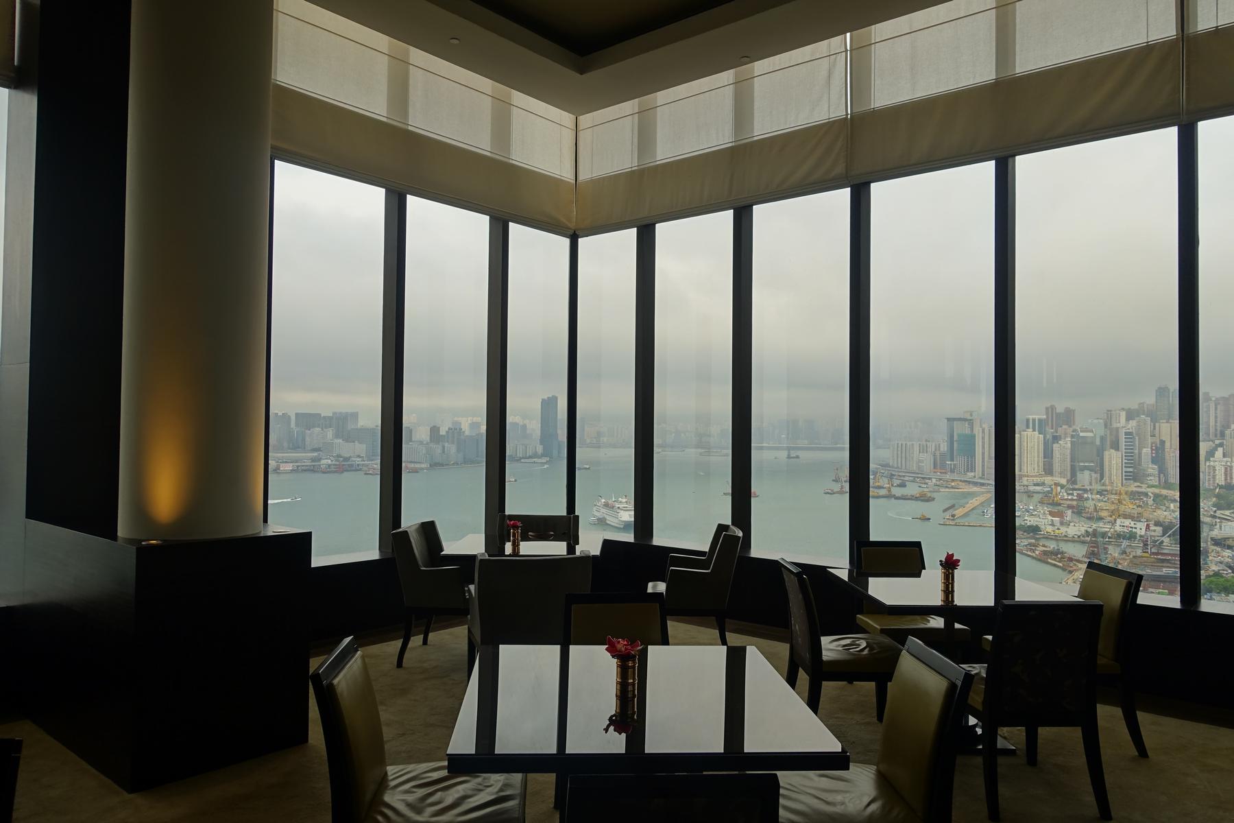 The renovated Grand Club Lounge features dark tables and chairs by large windows with a view of Hong Kong's city and Victoria Harbour.