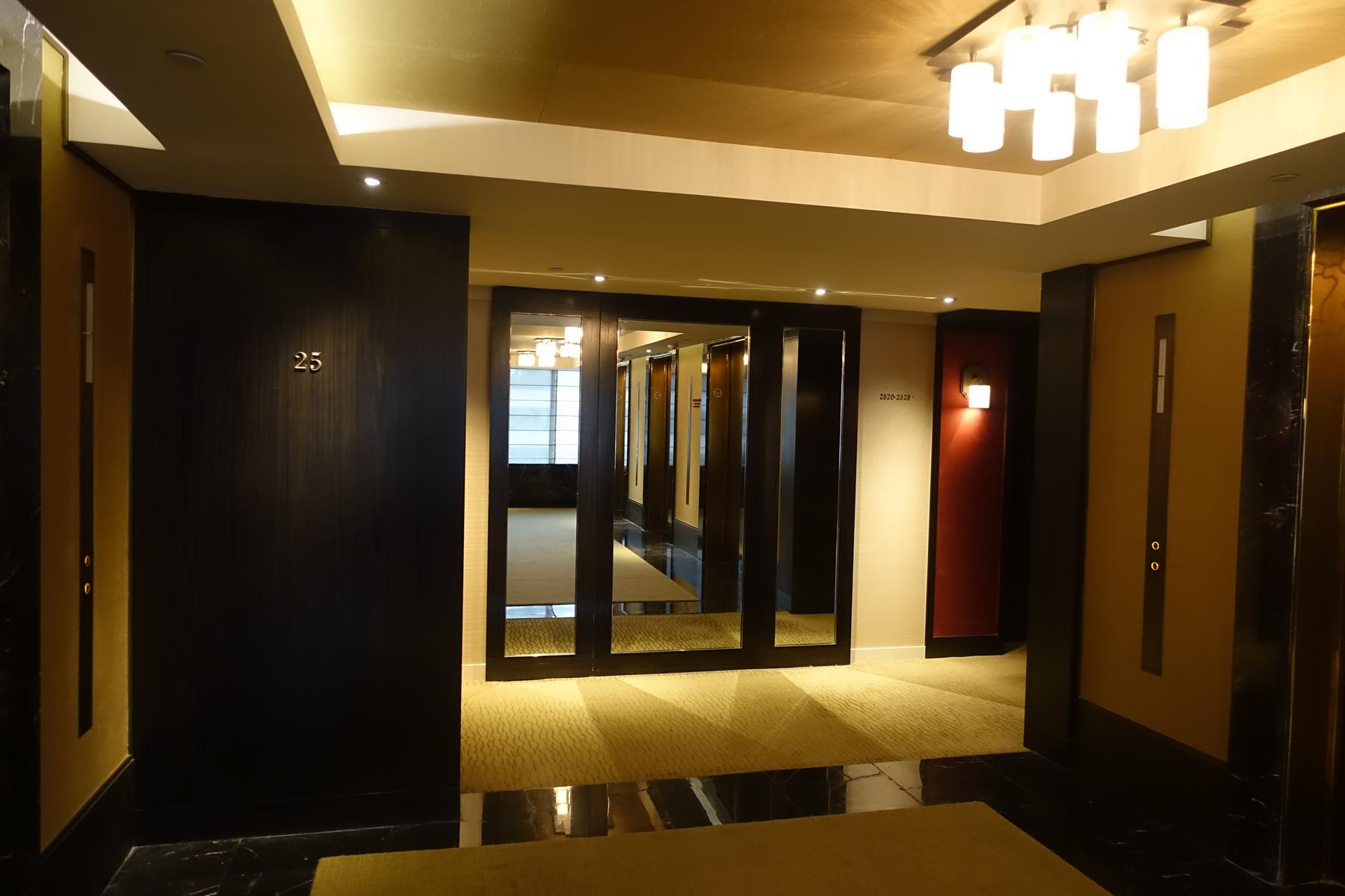 A modern hotel hallway featuring room number 25, reflective walls, and warm lighting.