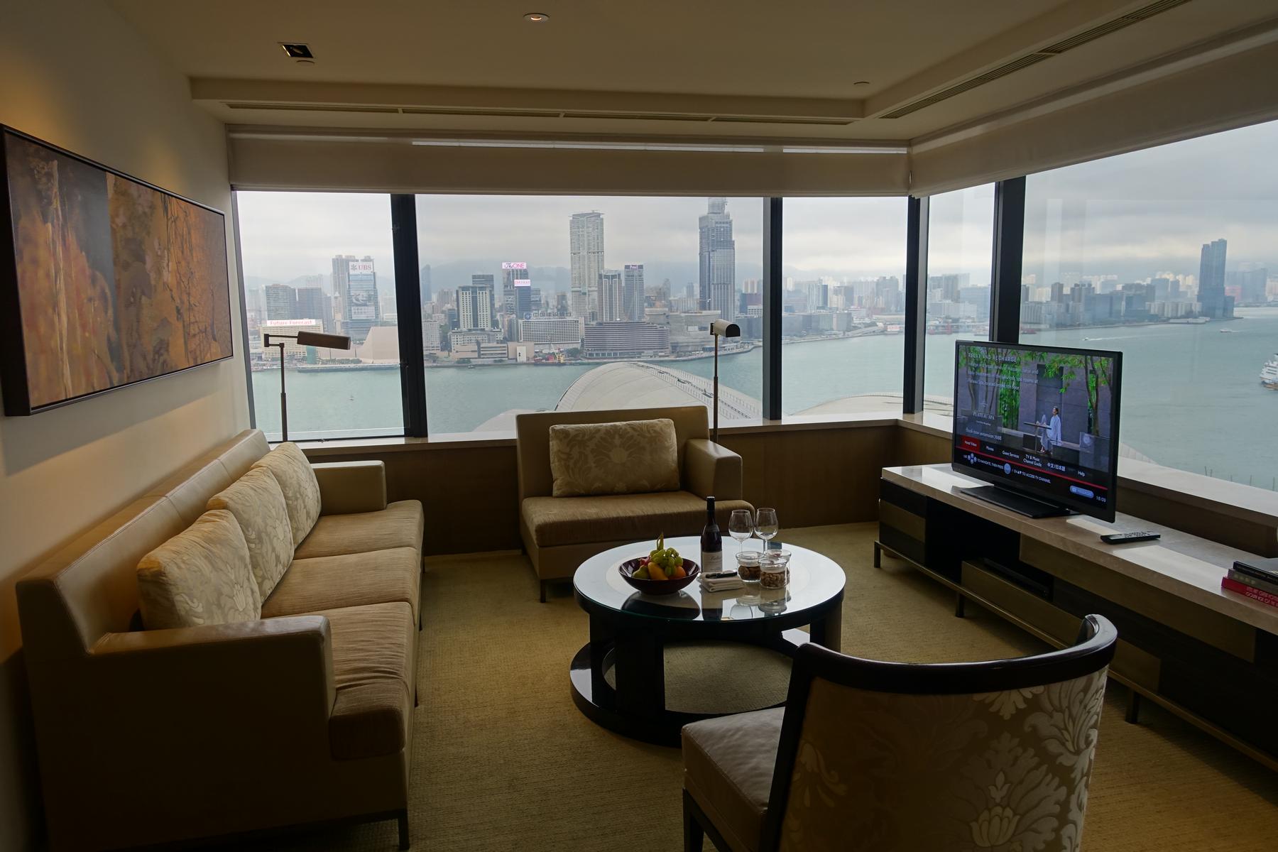 A Grand Hyatt Hong Kong Grand Suite living room with a panoramic view of the city skyline and harbor from a large window.