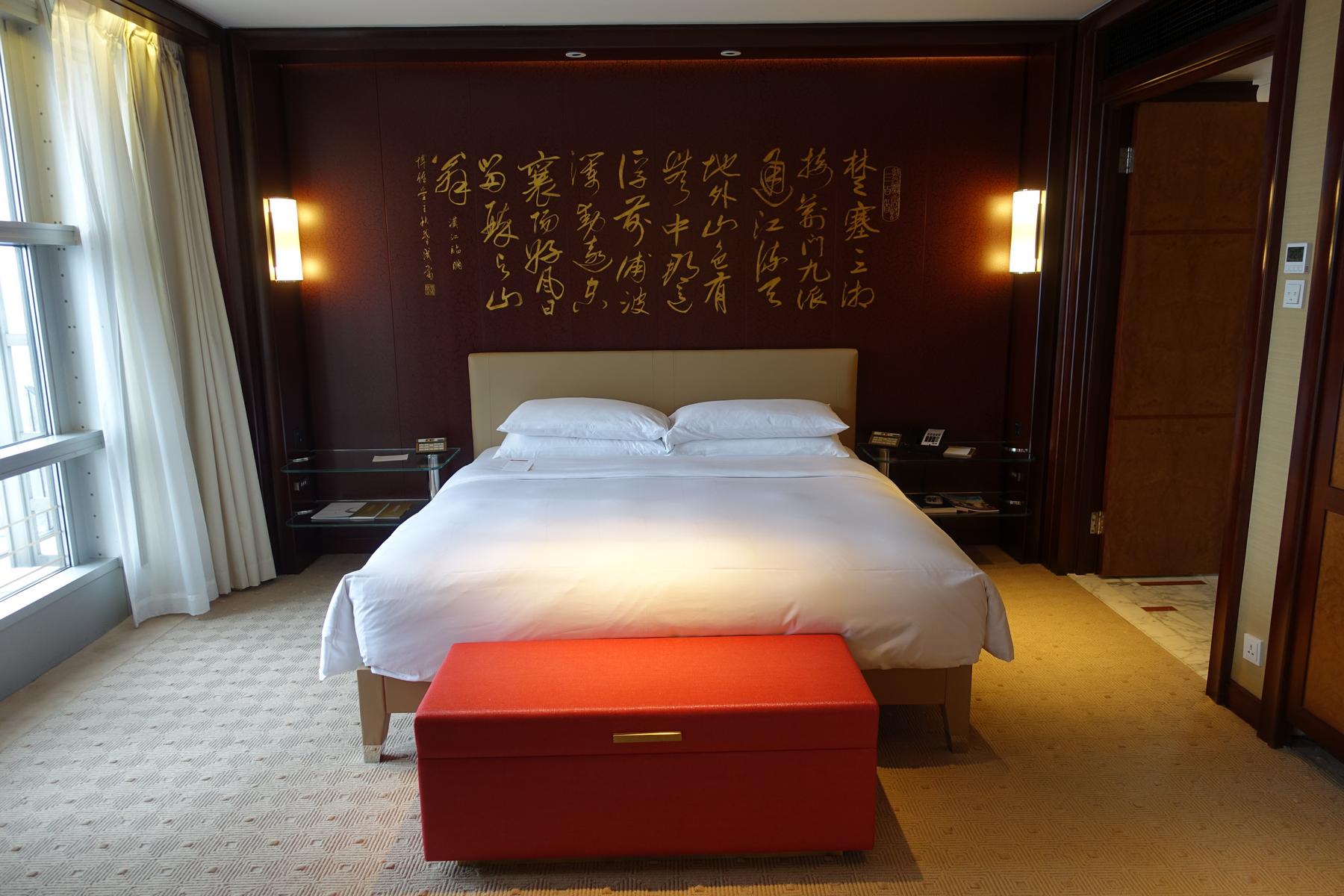Grand Hyatt Shanghai hotel room with a bed, red bench, and a headboard wall featuring gold Chinese calligraphy.