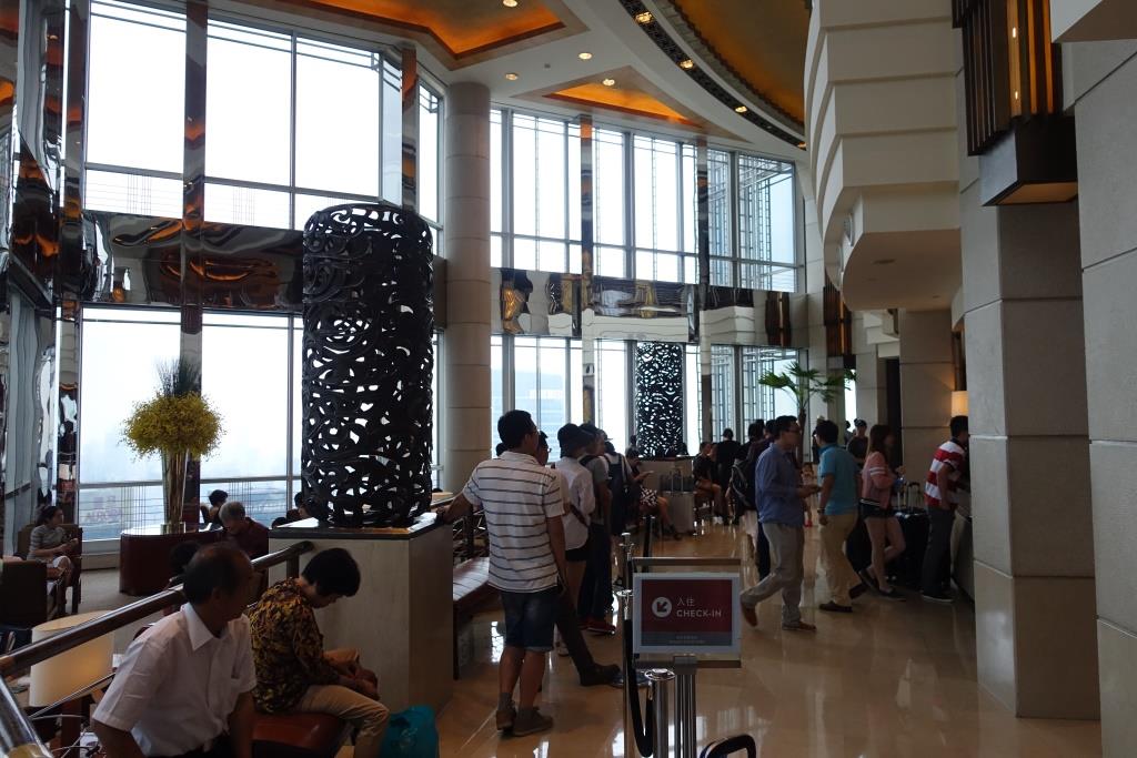 Guests gather in the modern, spacious lobby of the Grand Hyatt Shanghai, featuring floor-to-ceiling windows and ornate decor.