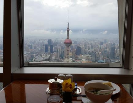 A meal on a table in front of a window overlooking the Shanghai city skyline and the Oriental Pearl TV Tower.