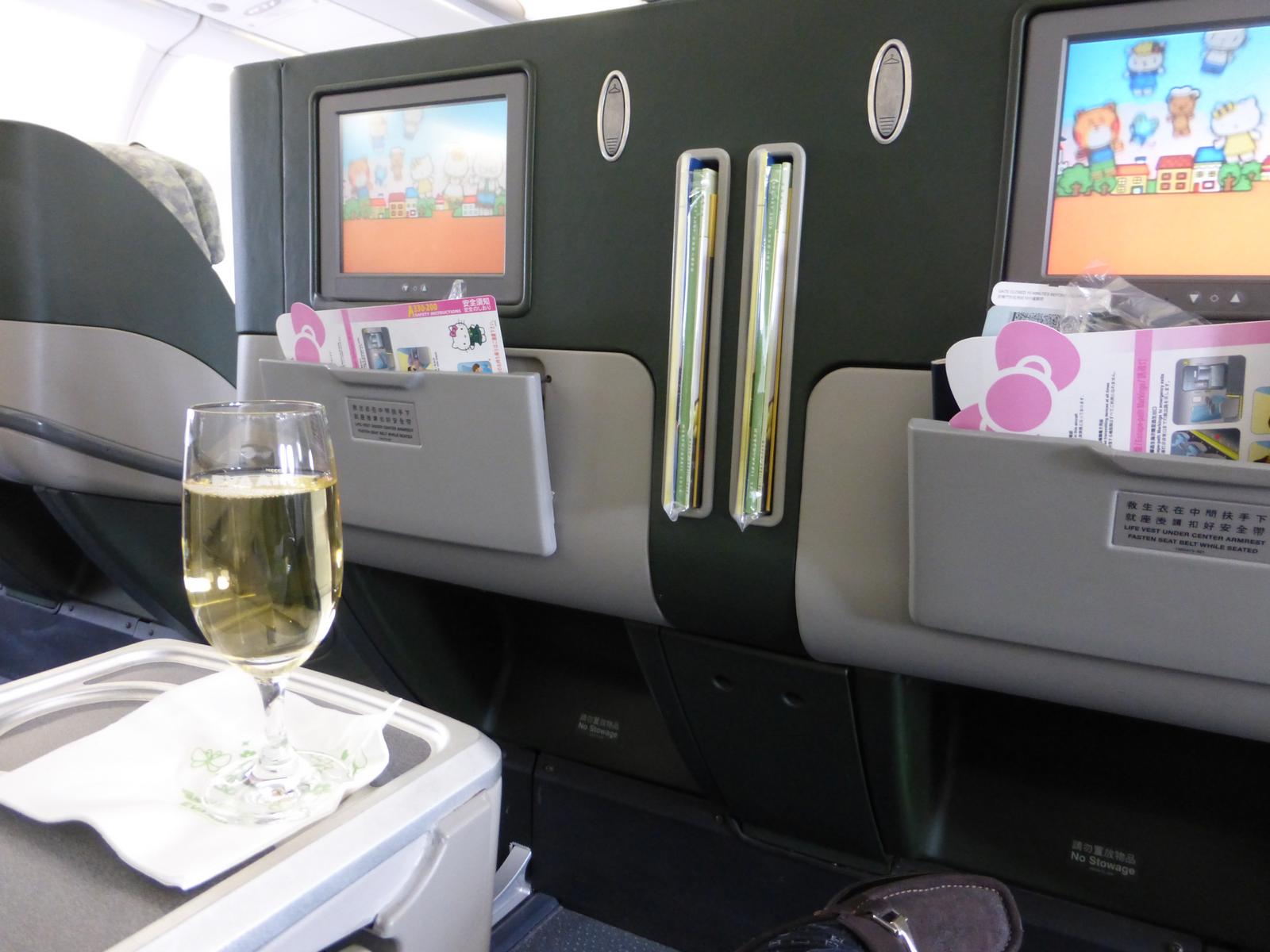 A glass of champagne on a tray in an Eva Air Hello Kitty business class cabin, with themed entertainment screens.