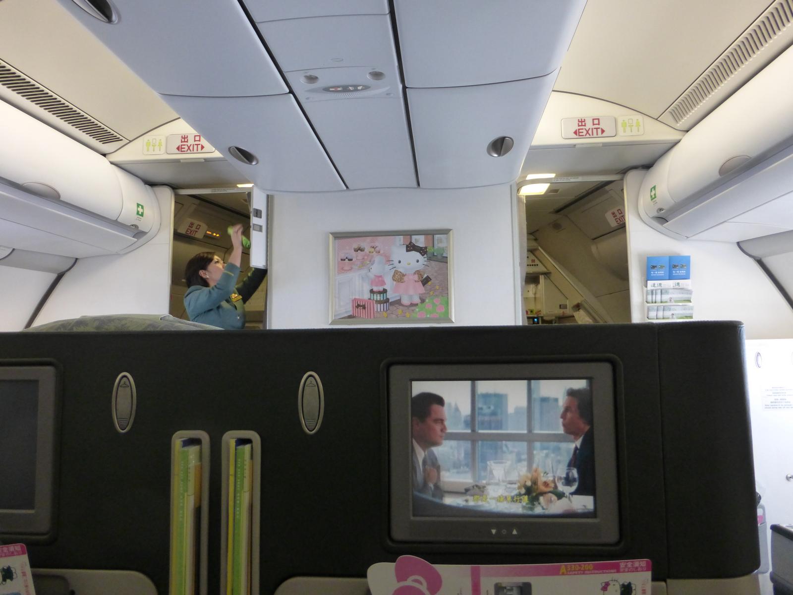 An Eva Air Hello Kitty business class cabin with a Hello Kitty picture on the bulkhead and a movie playing on an in-flight screen.