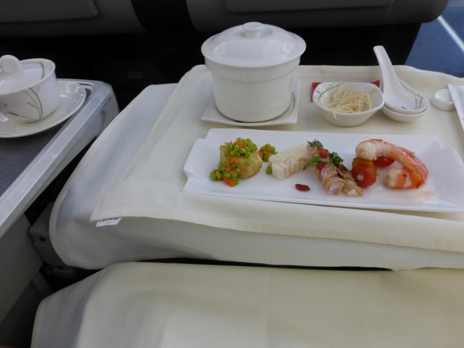 In-flight business class meal with shrimp, appetizers, and soup served on a white tablecloth.