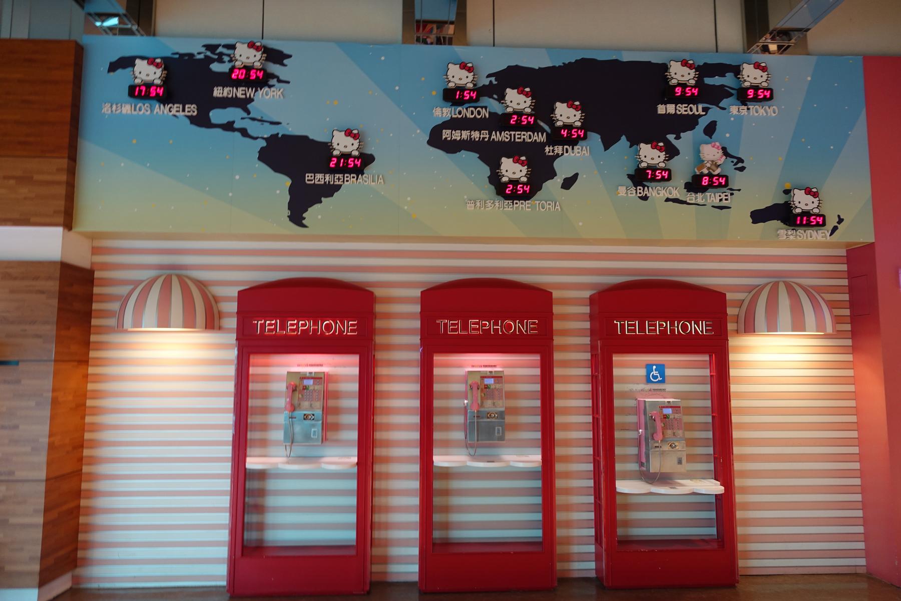 A Hello Kitty world map with clocks displayed above three red telephone booths in the themed airport lounge.