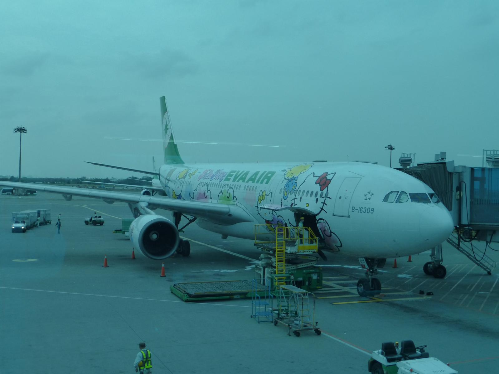 Eva Air Hello Kitty themed plane parked at an airport gate with a jet bridge attached.