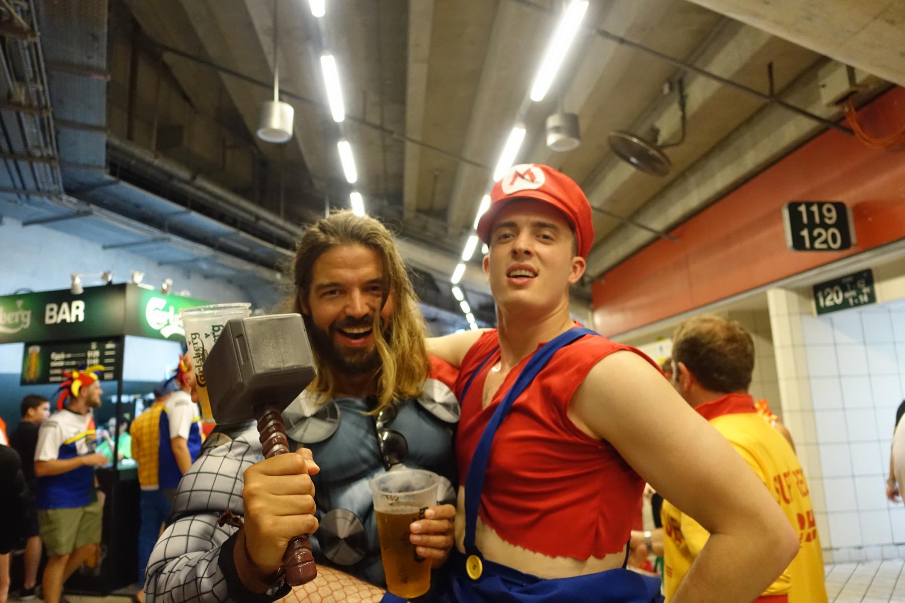 Two men in Thor and Mario costumes hold drinks and smile at the Hong Kong Rugby Sevens.