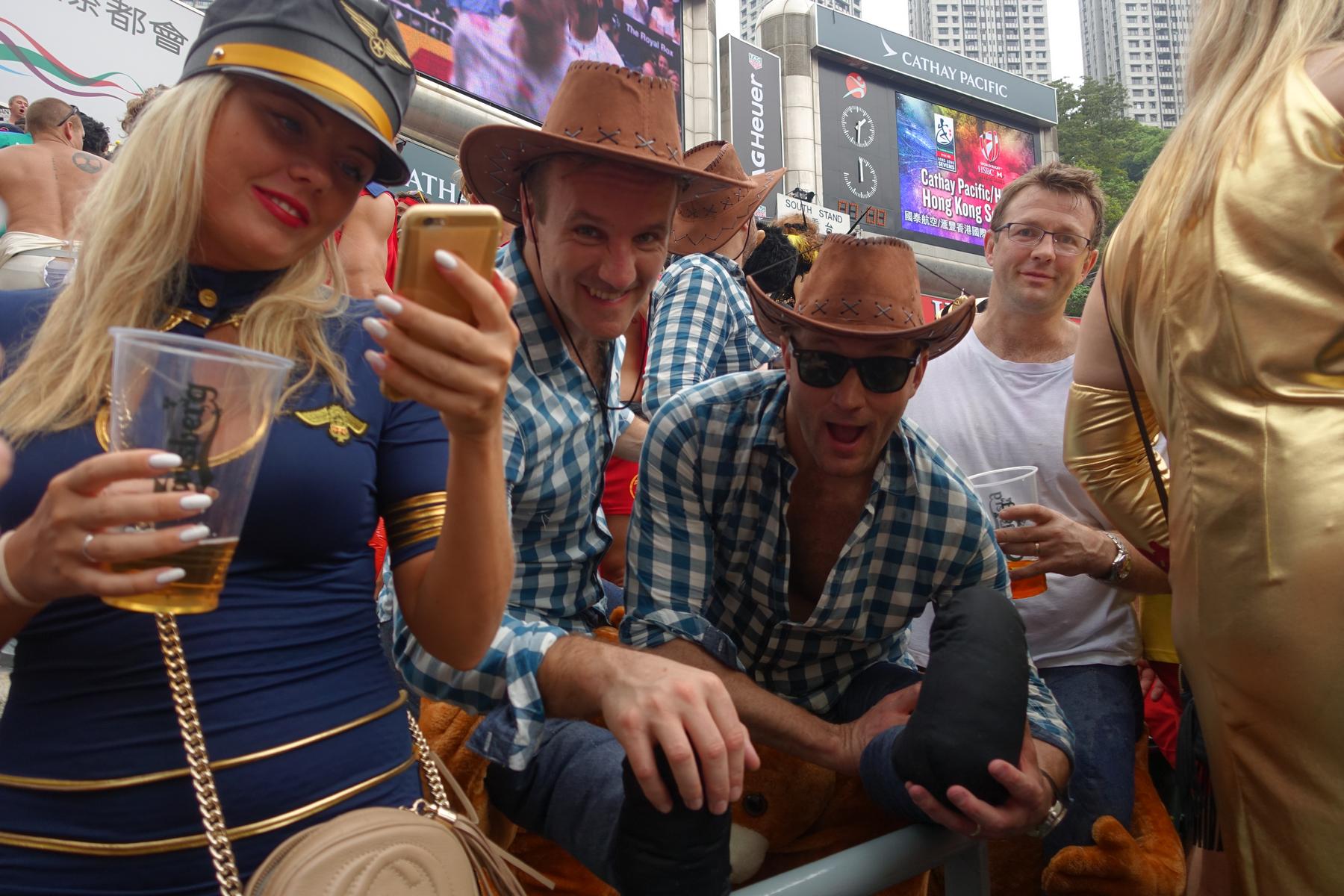 A woman in a flight attendant costume and two men in cowboy hats hold drinks at the Hong Kong Rugby Sevens.