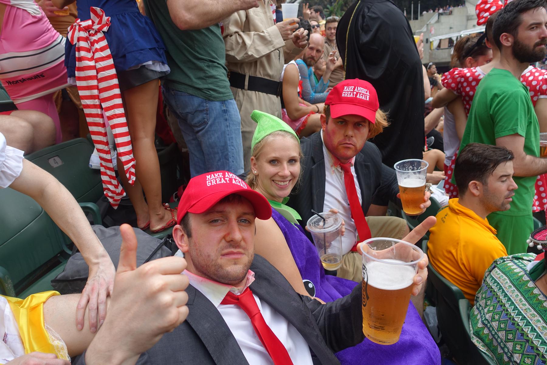 Costumed fans, including two men dressed as Donald Trump in "Make America Great Again" hats, enjoy drinks at the Rugby Sevens.