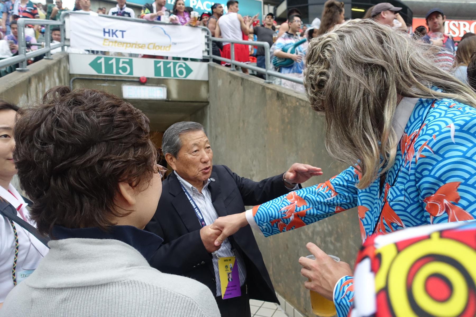 An older man talks to a person wearing a blonde wig and a blue kimono with koi fish at the Hong Kong Rugby Sevens.