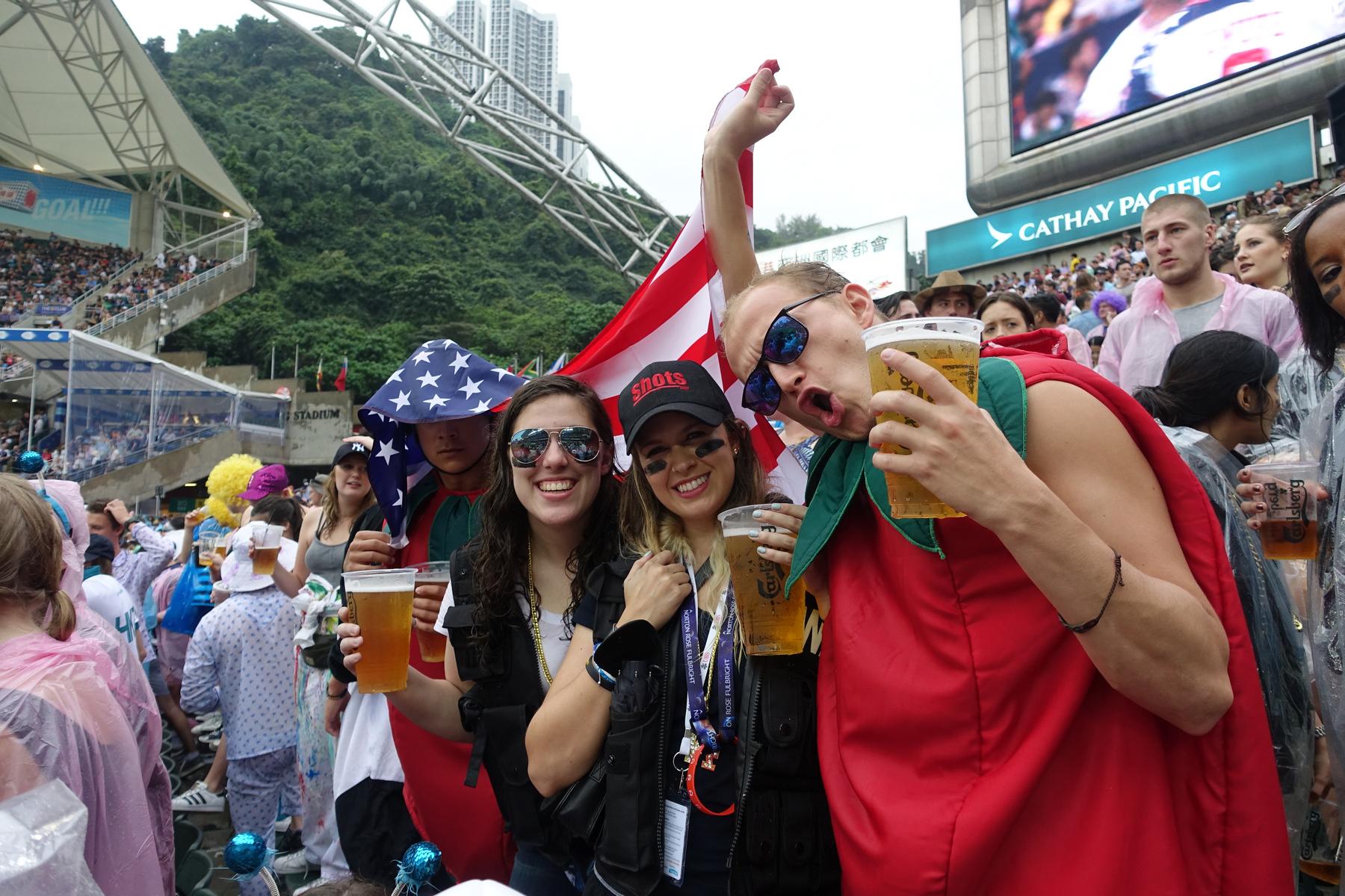 A group of cheerful fans holding beers and wearing festive costumes at the Hong Kong Rugby Sevens South Stand.