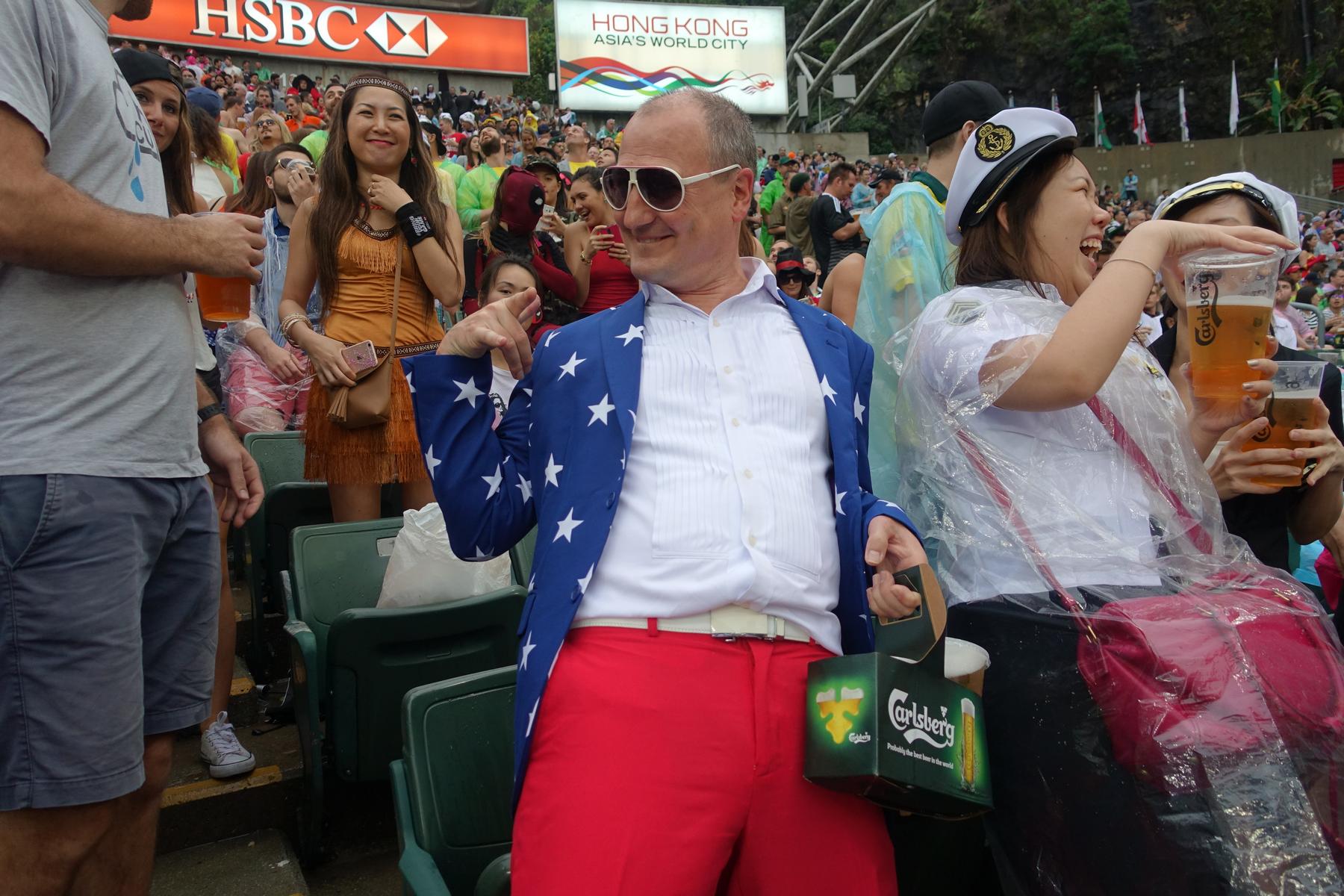 Fans in costumes, including a man in a stars-and-stripes suit, drink beer at the lively Hong Kong Rugby Sevens South Stand.