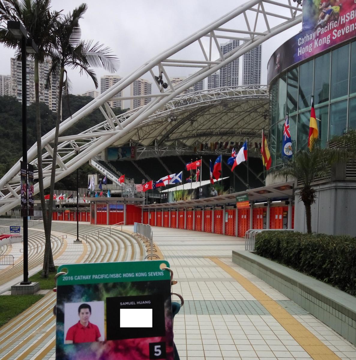 A 2016 Hong Kong Rugby Sevens pass is held at the stadium entrance, with international flags flying.