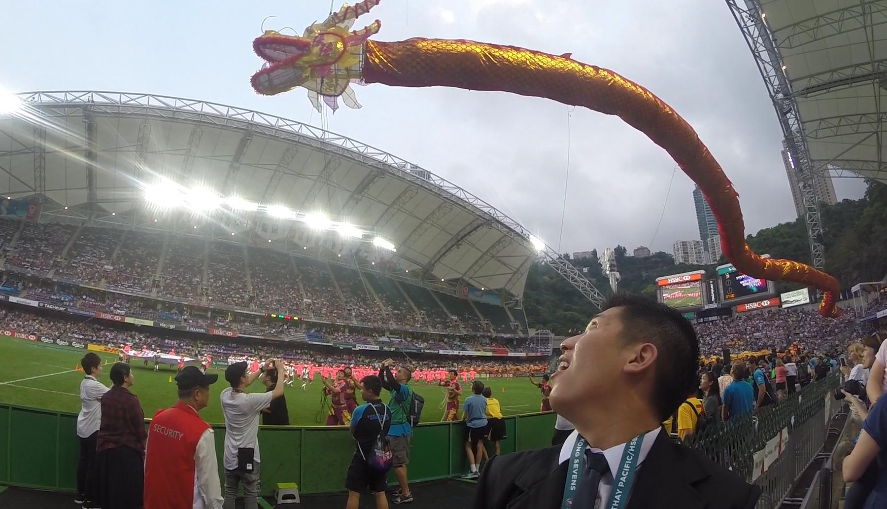 A man looks up in awe at a giant golden dragon floating over a crowded stadium during the Hong Kong Rugby Sevens.