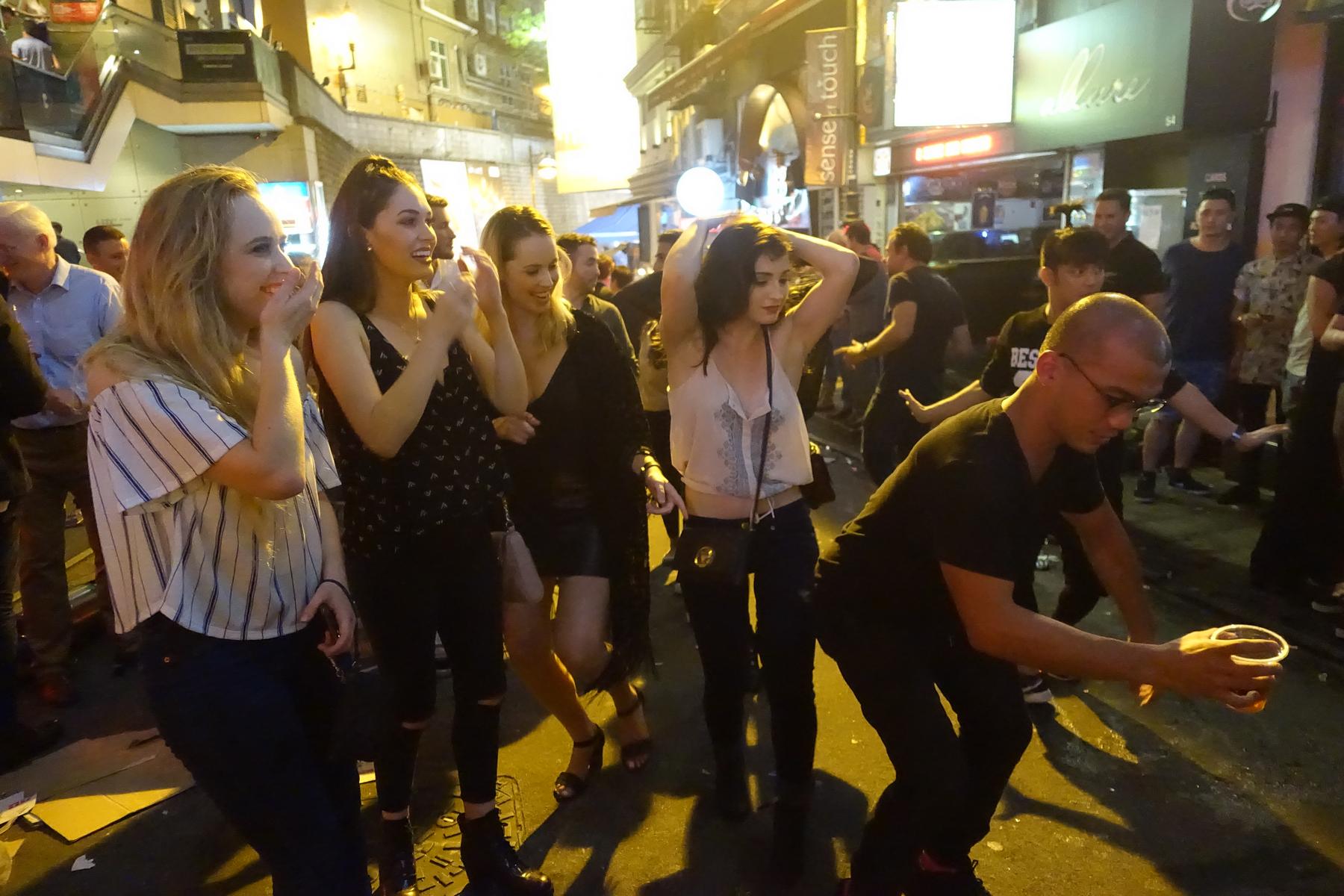 A group of people enjoying a lively street party scene in Hong Kong at night.