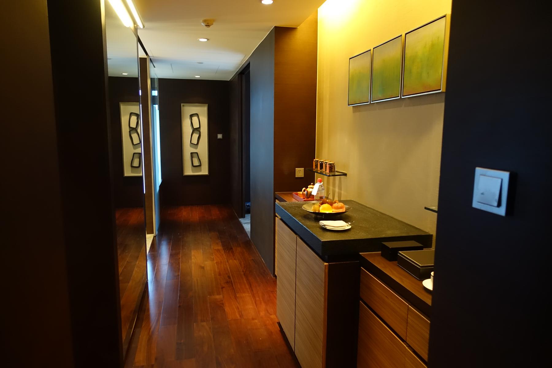 A modern hotel suite hallway featuring a fruit and beverage counter, dark wood floors, and wall decorations.