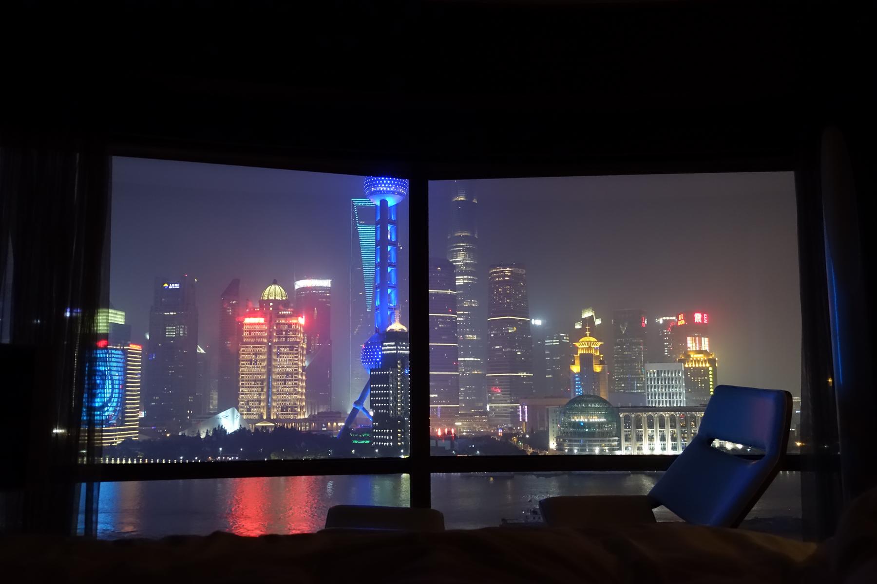 Panoramic nighttime view of the Shanghai skyline, including the Oriental Pearl TV Tower, from a hotel window.