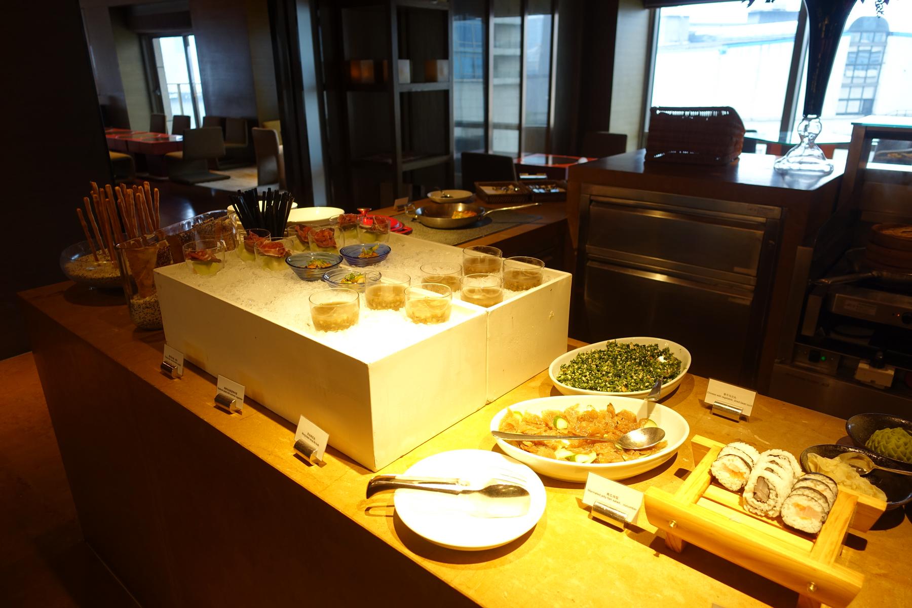 A buffet spread in a club lounge featuring sushi, salads, and individual chilled dishes.