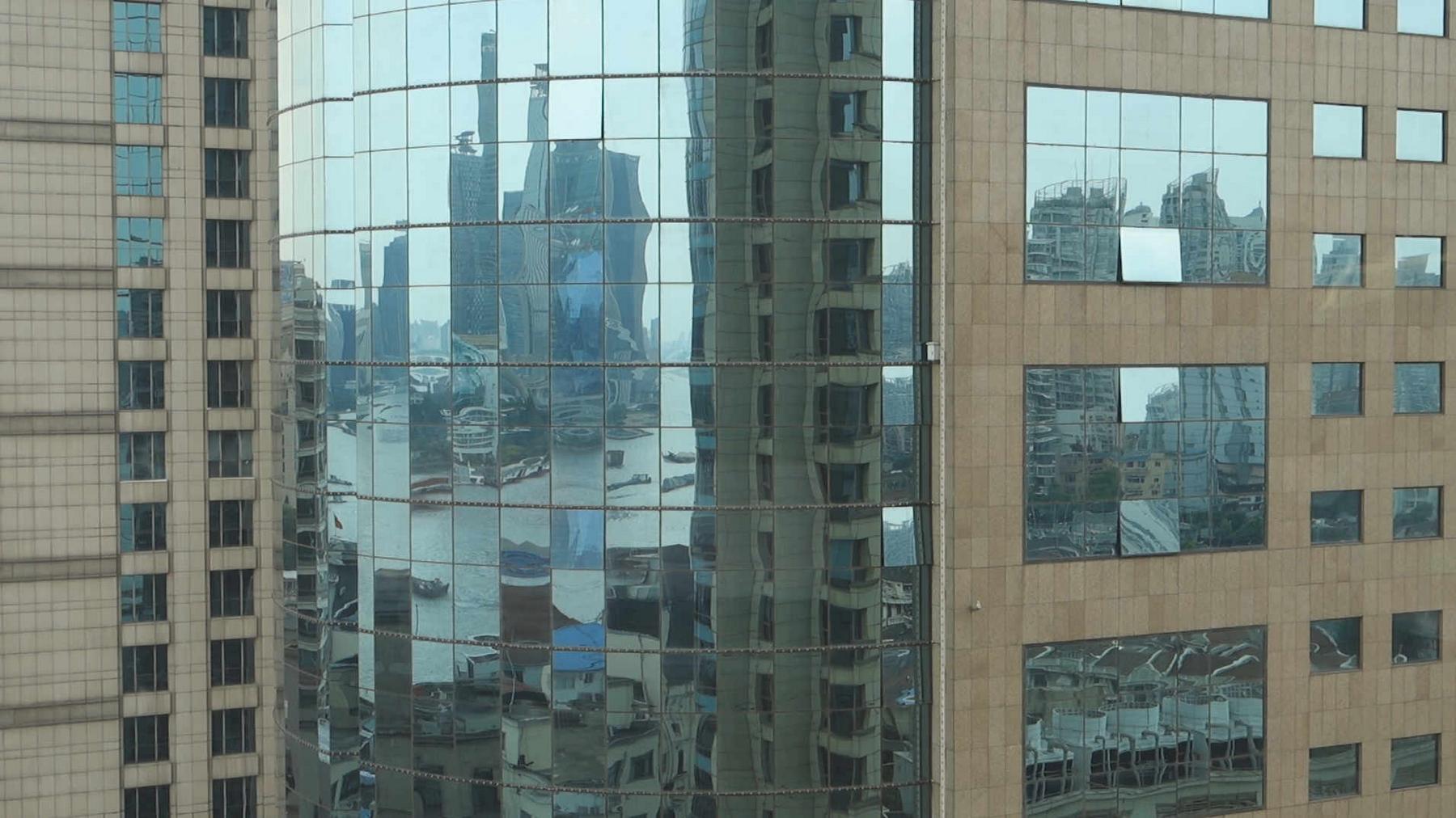 Glass facade of a building reflecting the Shanghai skyline and Huangpu River.