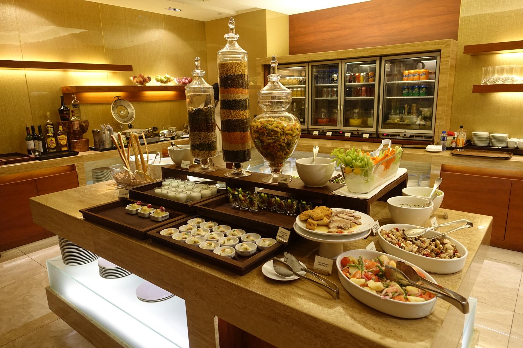 A hotel buffet table displaying a variety of appetizers, salads, desserts, and drinks, including decorative jars of grains.