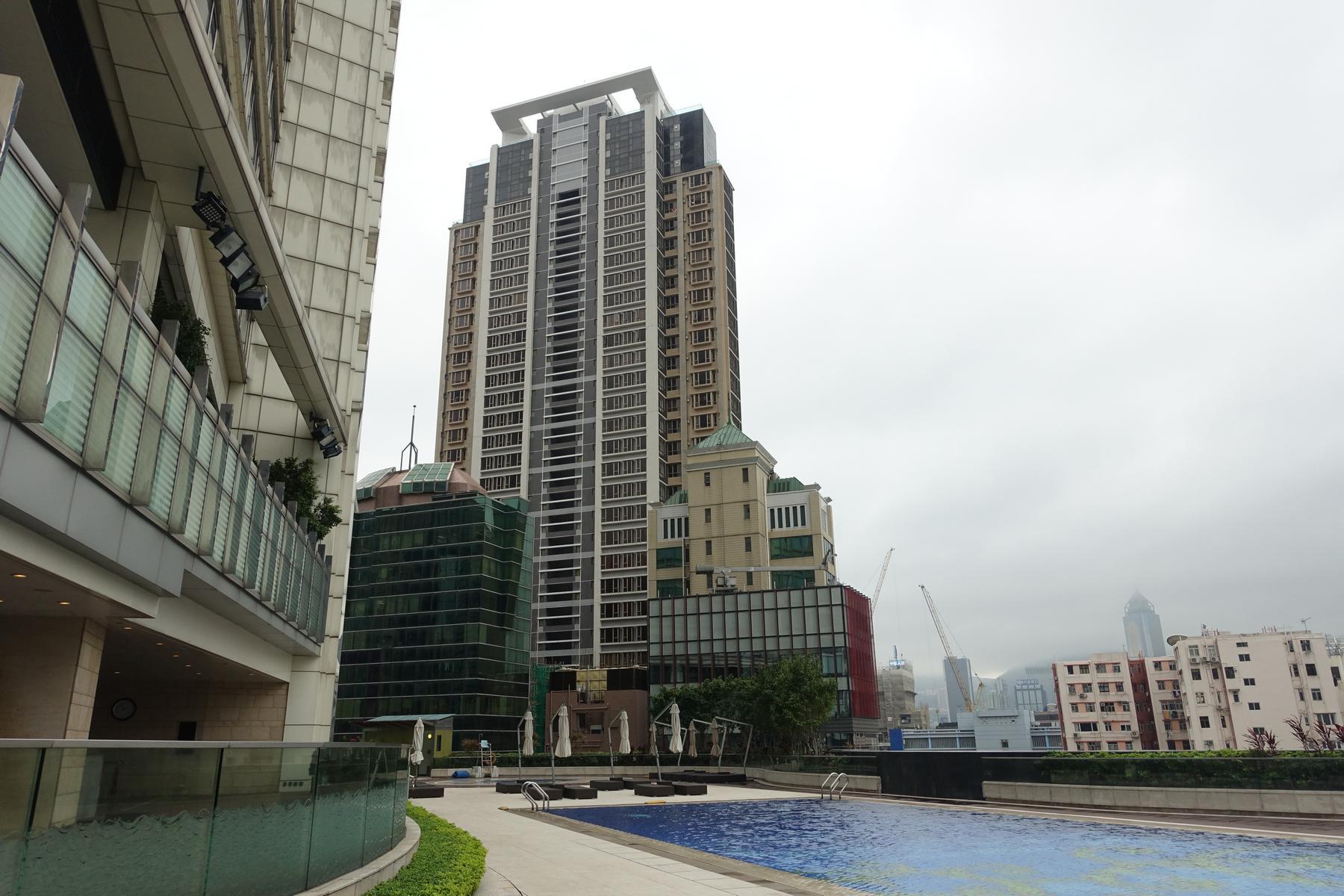 Outdoor swimming pool at the Hyatt Regency Hong Kong surrounded by tall buildings under a cloudy sky.