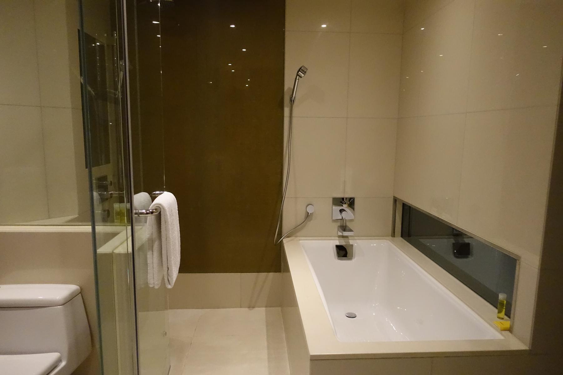 Modern hotel bathroom with a deep bathtub, handheld shower, and glass shower enclosure.