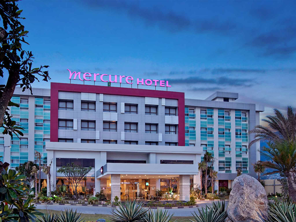 Exterior of a Mercure Hotel at dusk with tropical landscaping.