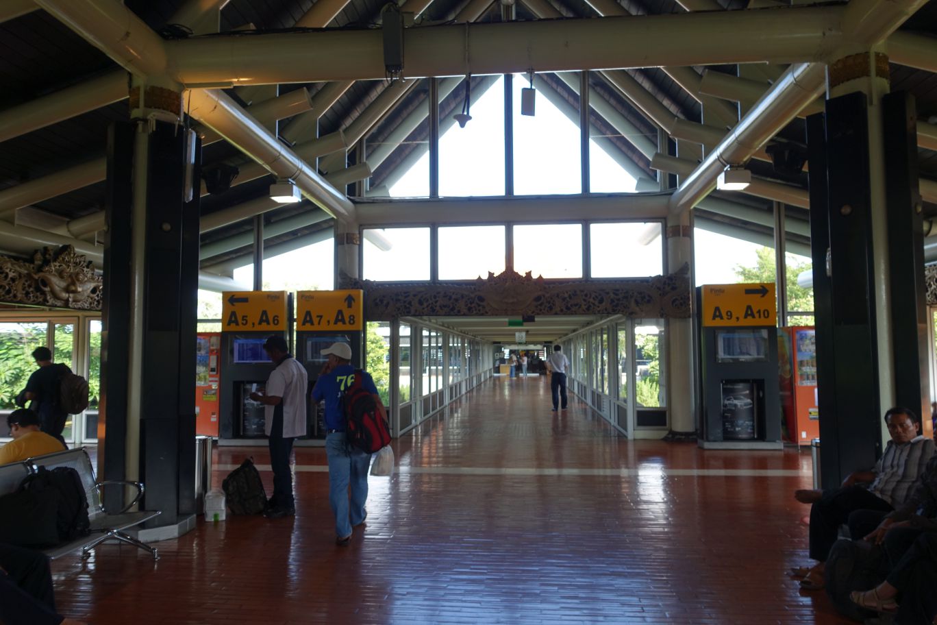 A bright, vaulted Indonesian airport terminal with traditional carved details, large windows, and gate signs.