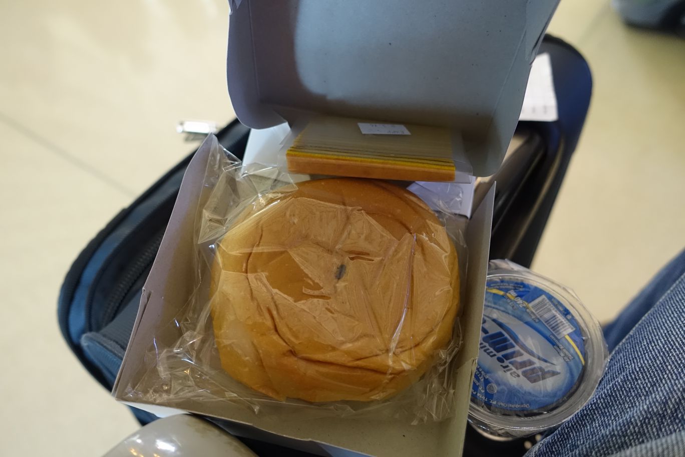 A Lion Air in-flight snack box containing a bun, bottled water, and papers.