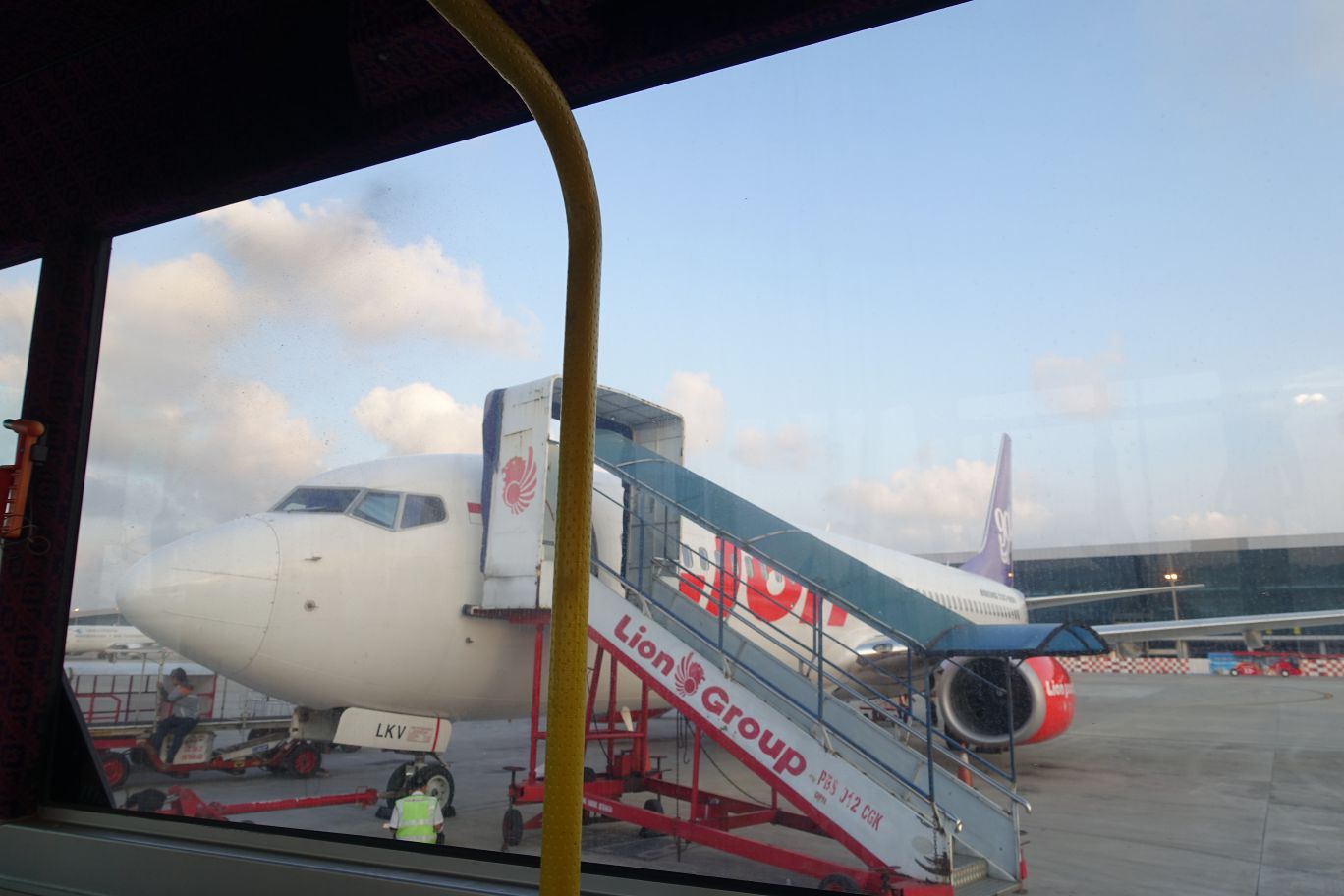 A Lion Air plane on the tarmac with boarding stairs attached, viewed from inside a window.