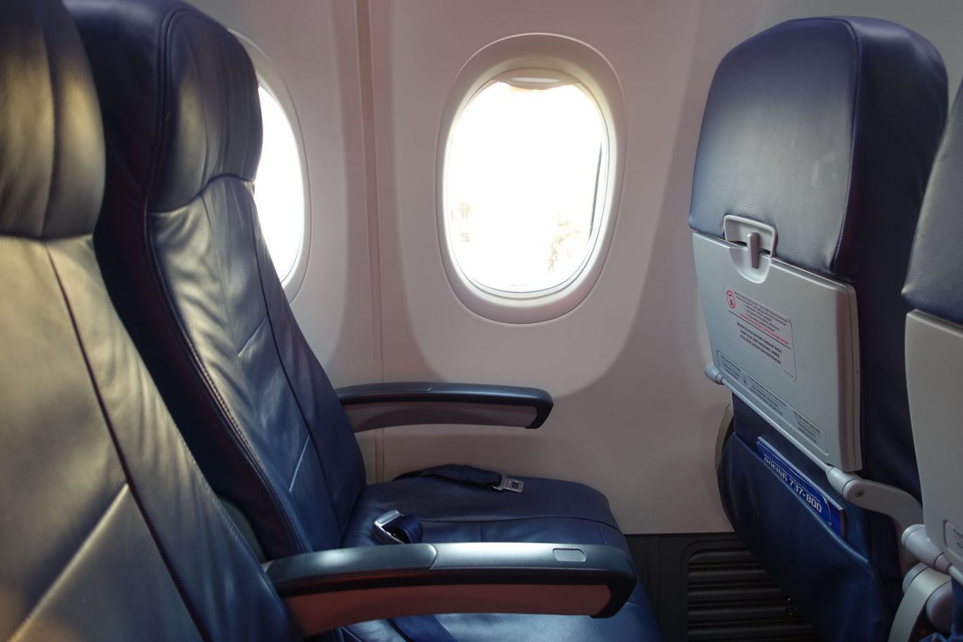 Empty blue seats and bright windows inside a Lion Air airplane cabin.