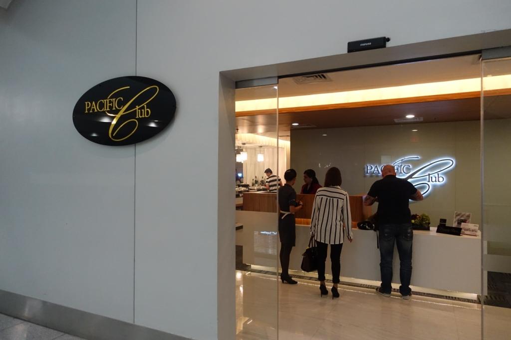 Entrance to the Pacific Club Lounge with its sign on the wall and a reception area visible through glass doors.