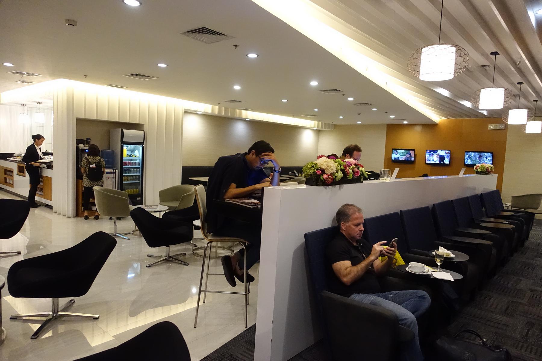 People relaxing and working in the Pacific Club Lounge at Manila Airport, featuring various seating and a refreshment counter.