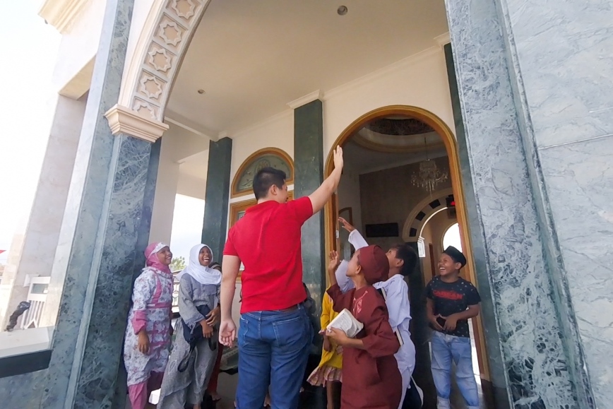 A man points upwards while children look on at an ornate building entrance.