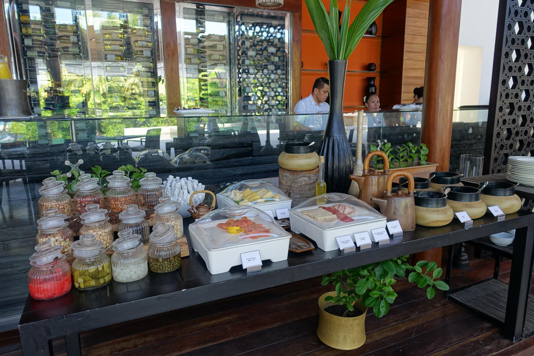 A luxurious breakfast buffet table at Park Hyatt Maldives, featuring jars of nuts, covered dishes of cold cuts, and various serving pots.
