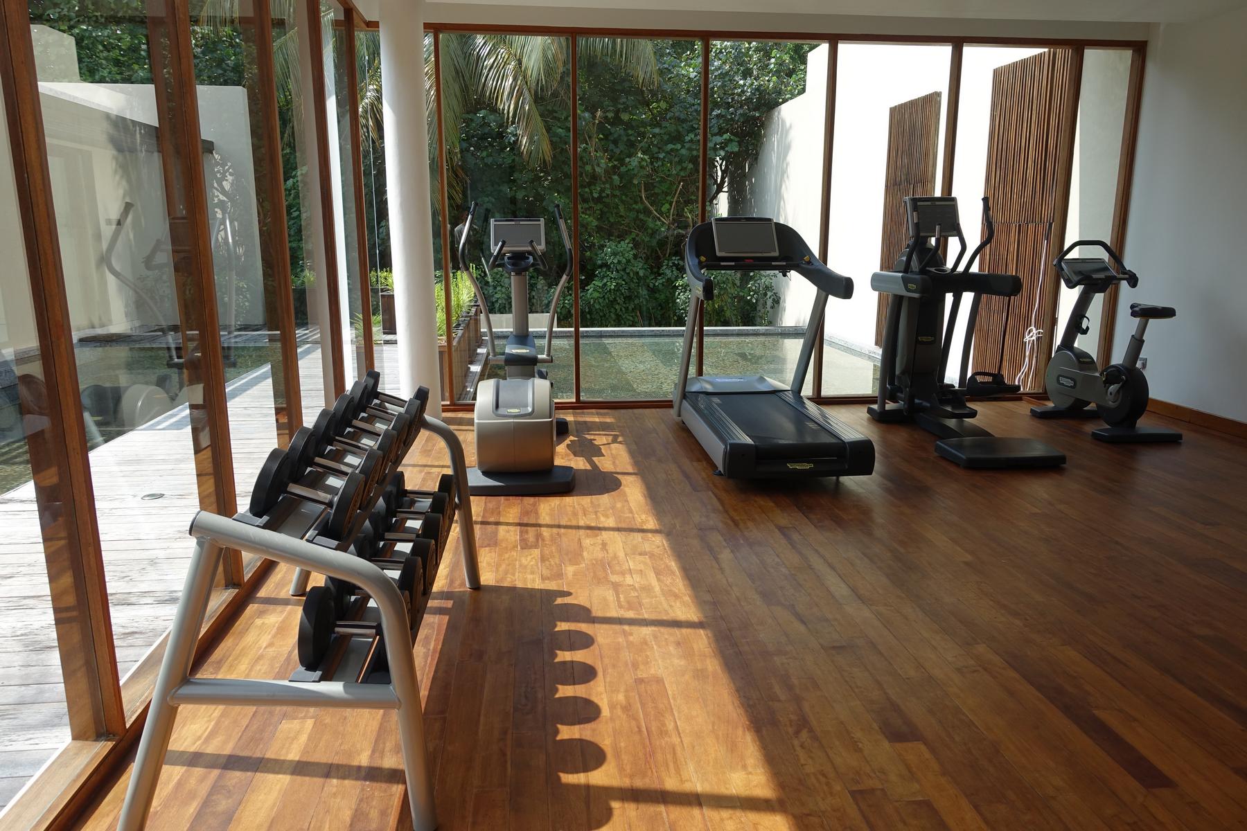 The Park Hyatt Maldives gym, with cardio machines and dumbbells, overlooks a tropical landscape and water feature.