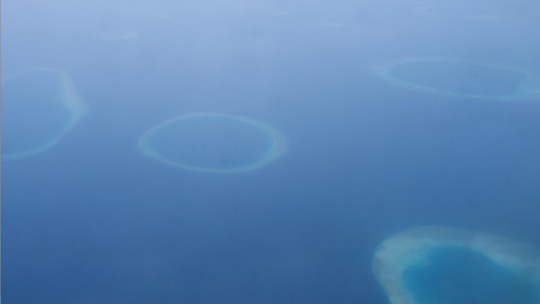 Aerial view of multiple circular atolls and coral reefs in the deep blue ocean.