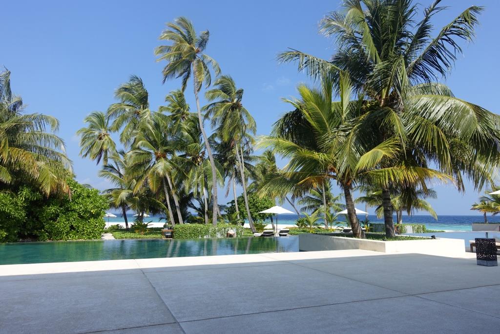 A large patio overlooks an infinity pool, palm trees, and the ocean at Park Hyatt Maldives.
