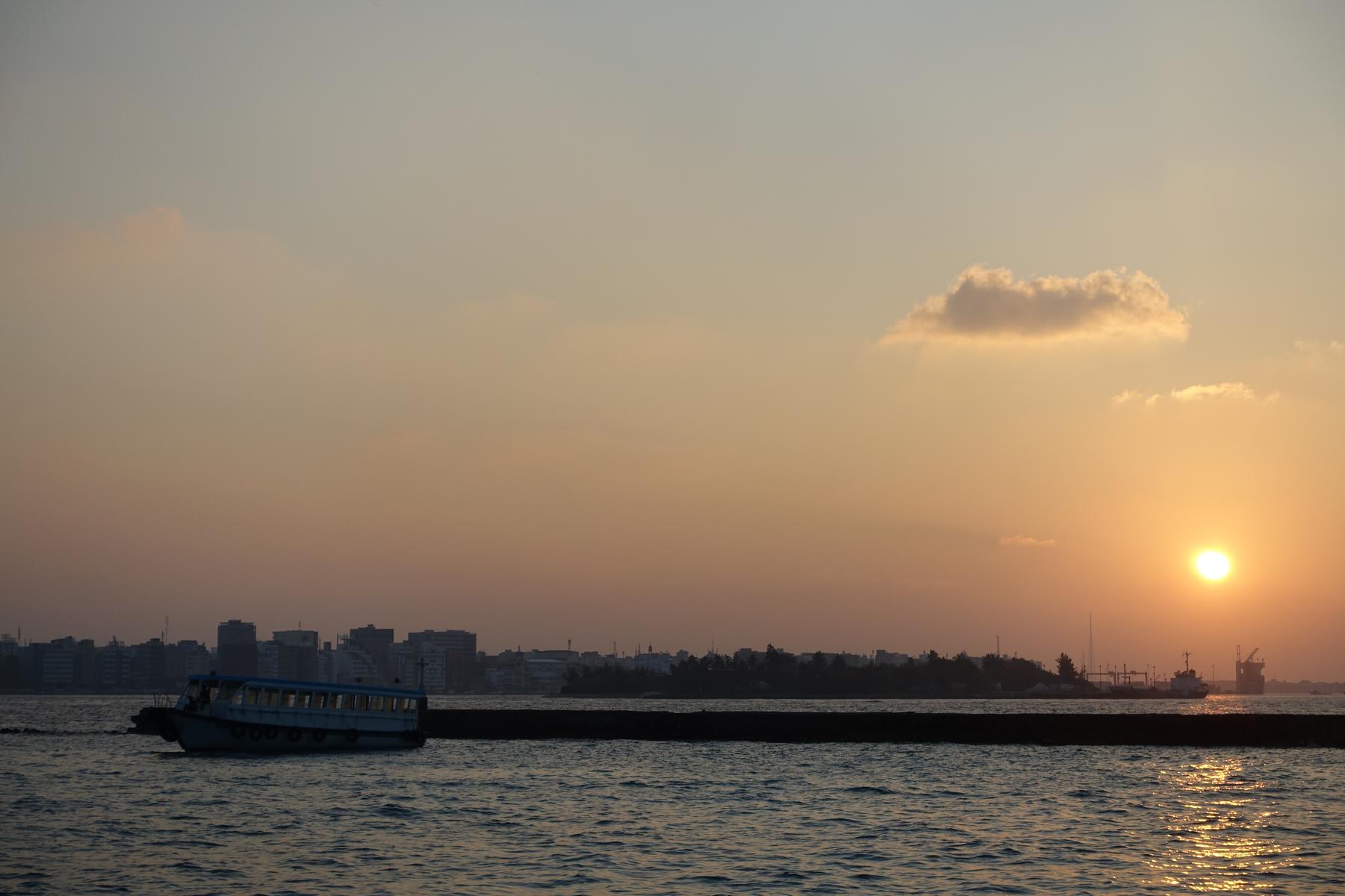A ferry boat on the water with the Male city skyline visible at sunset.