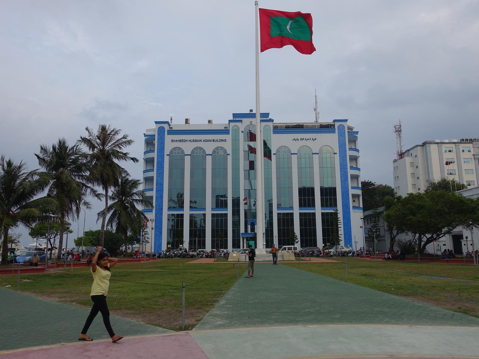 The Shaheedh Hussain Adam Building and the Maldives flag overlook a green park in Male.