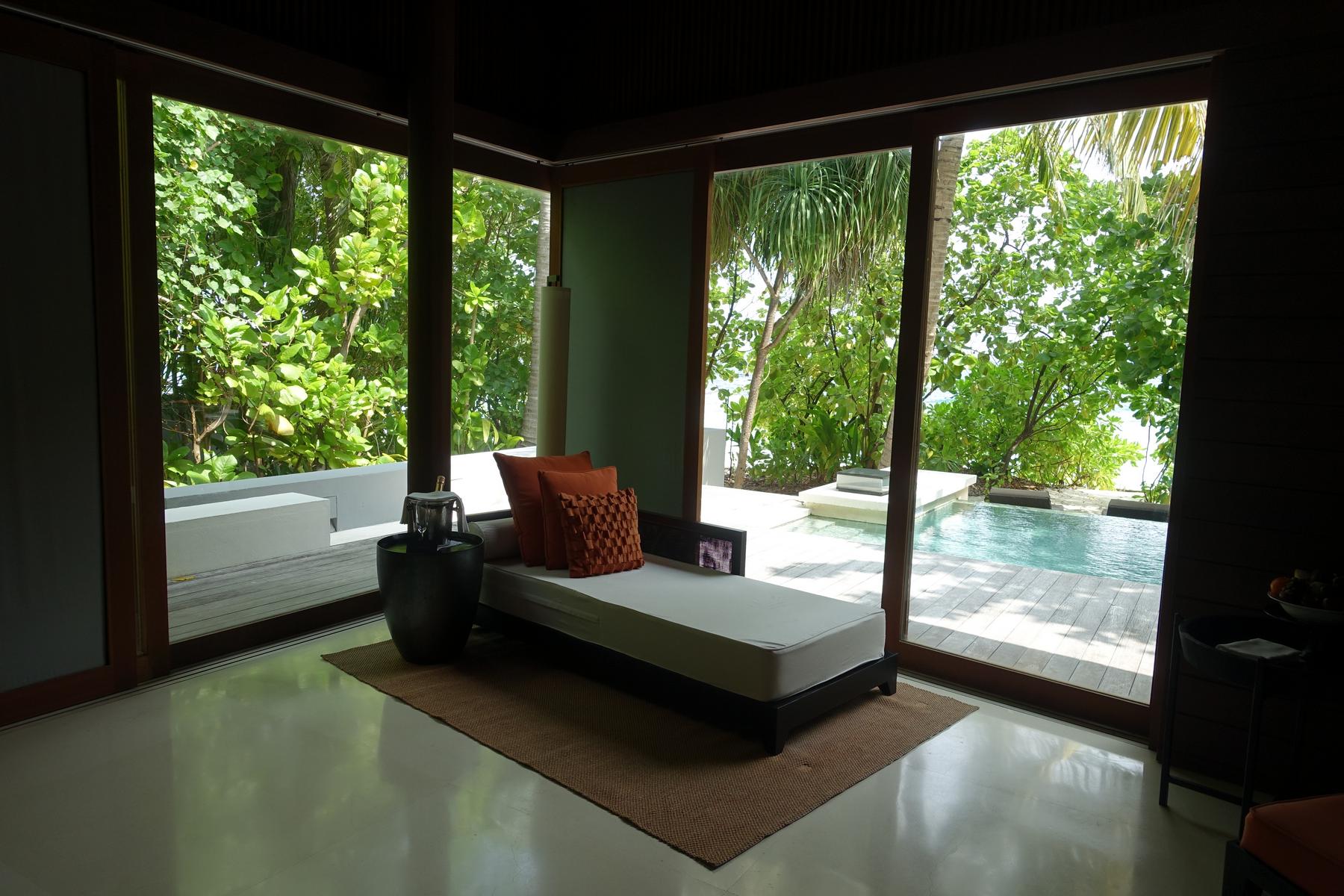 A villa interior with a daybed, large windows, a private pool, and lush tropical views of the ocean.