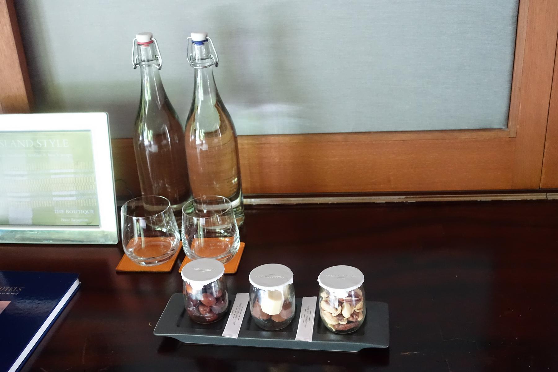 Two bottles of water, two glasses, and three jars of snacks are arranged on a dark wooden counter.