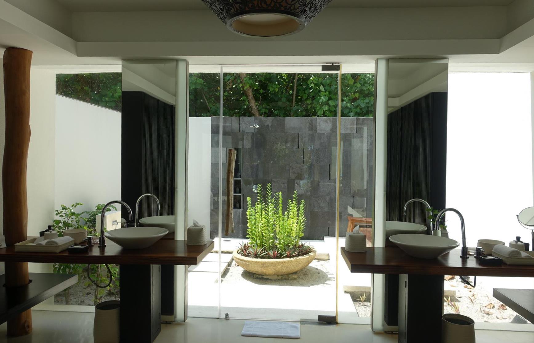Modern bathroom with dual sinks, leading to an outdoor shower and tropical courtyard.