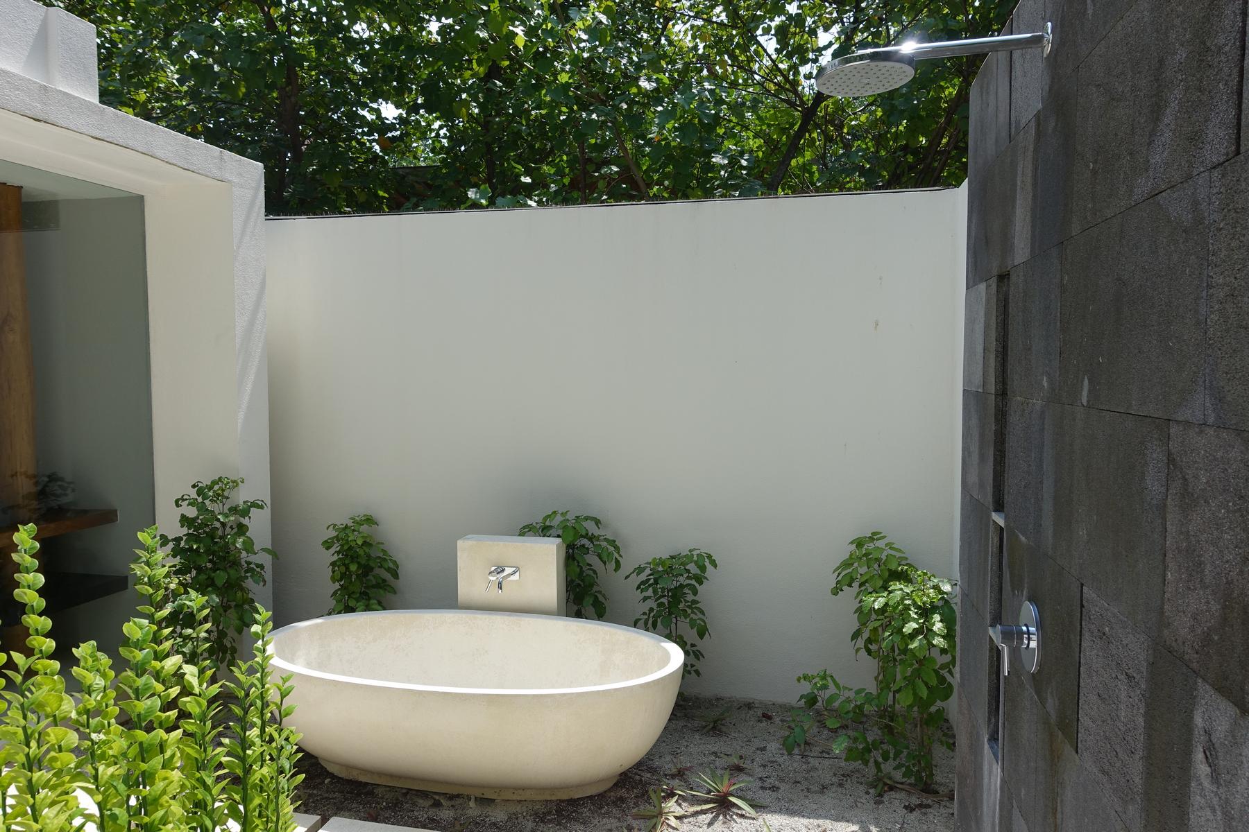 Outdoor bathroom with a freestanding tub, rain shower, and tropical plants at Park Hyatt Maldives.